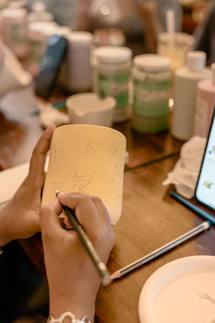 Close-up of hands painting designs on a ceramic mug, showcasing creativity and art in a workshop setting.
