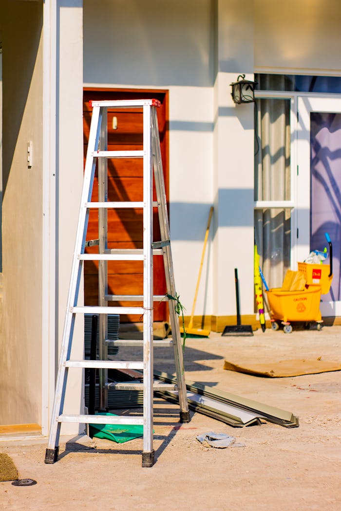 An outdoor home renovation scene featuring a ladder and various tools indicating ongoing construction work.