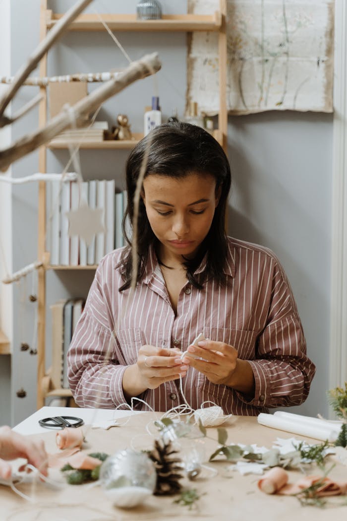 A woman in a striped shirt crafts handmade Christmas decorations using natural materials.