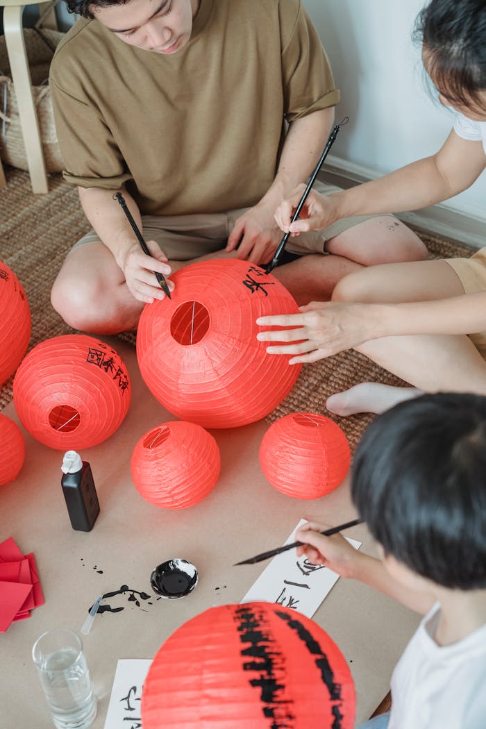 Family engaging in painting red paper lanterns together indoors, fostering creativity and togetherness.
